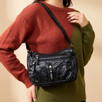 Person wearing a black leather crossbody bag with a neutral background