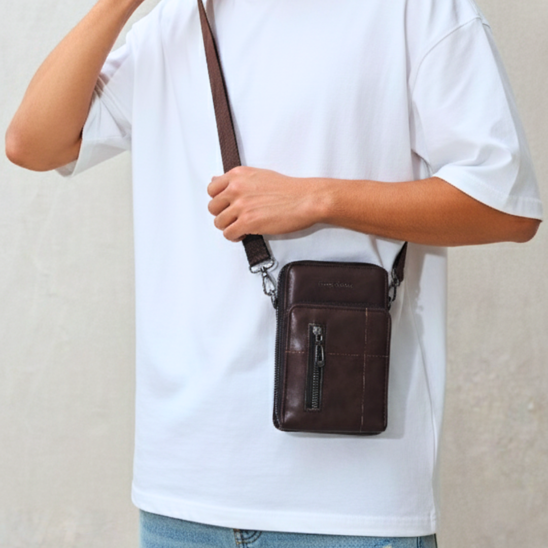 Person holding a brown leather crossbody bag against a plain background