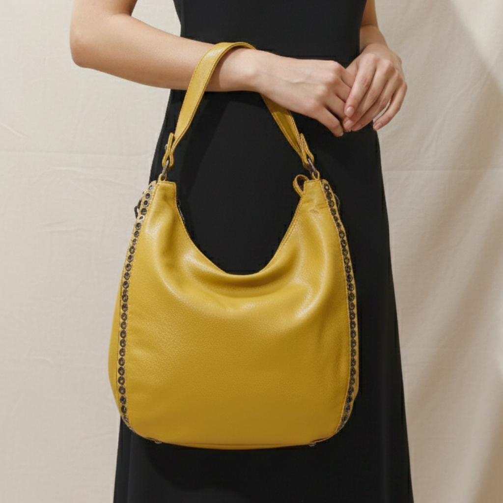 Yellow handbag with black chain detail held by a person wearing a black dress against a neutral background