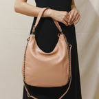 Person holding a beige handbag with a chain detail against a neutral background