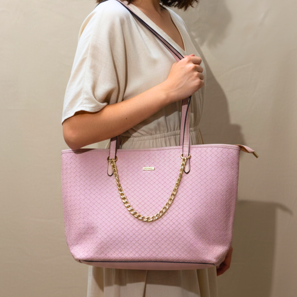 Pink handbag with gold chain held by a person against a neutral background
