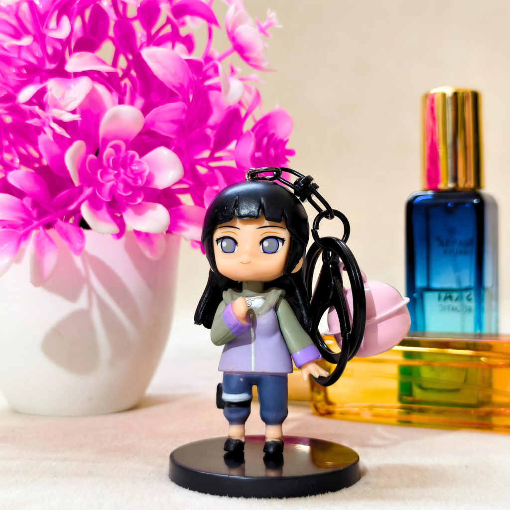 Small figurine of a character holding a keychain with pink flowers and perfume bottles in the background.