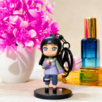 Small figurine of a character holding a keychain with pink flowers and perfume bottles in the background.