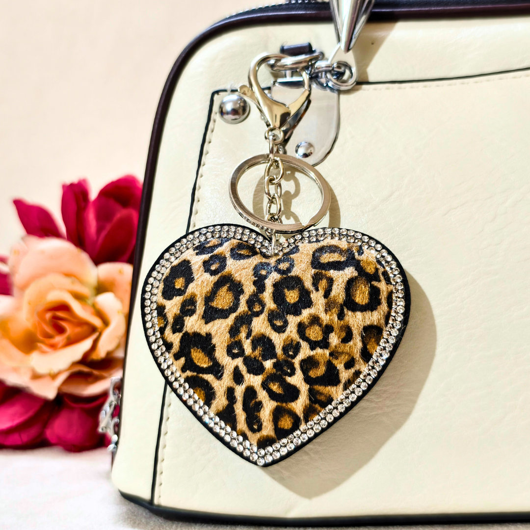 Leopard print heart-shaped keychain on a beige handbag with flowers in the background