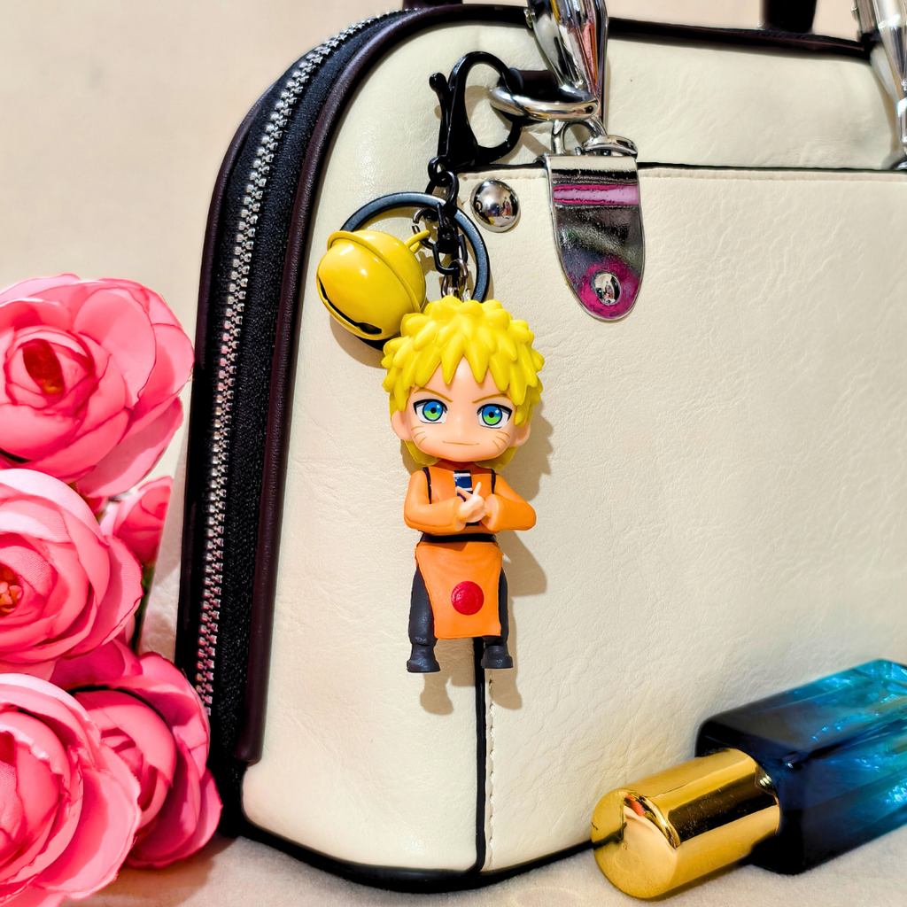 Keychain with a character attached to a handbag next to pink flowers and a blue bottle.