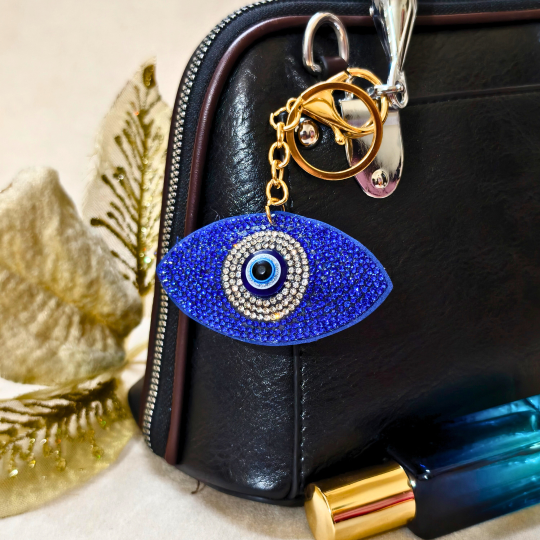 Blue evil eye keychain on a black leather bag with decorative elements.