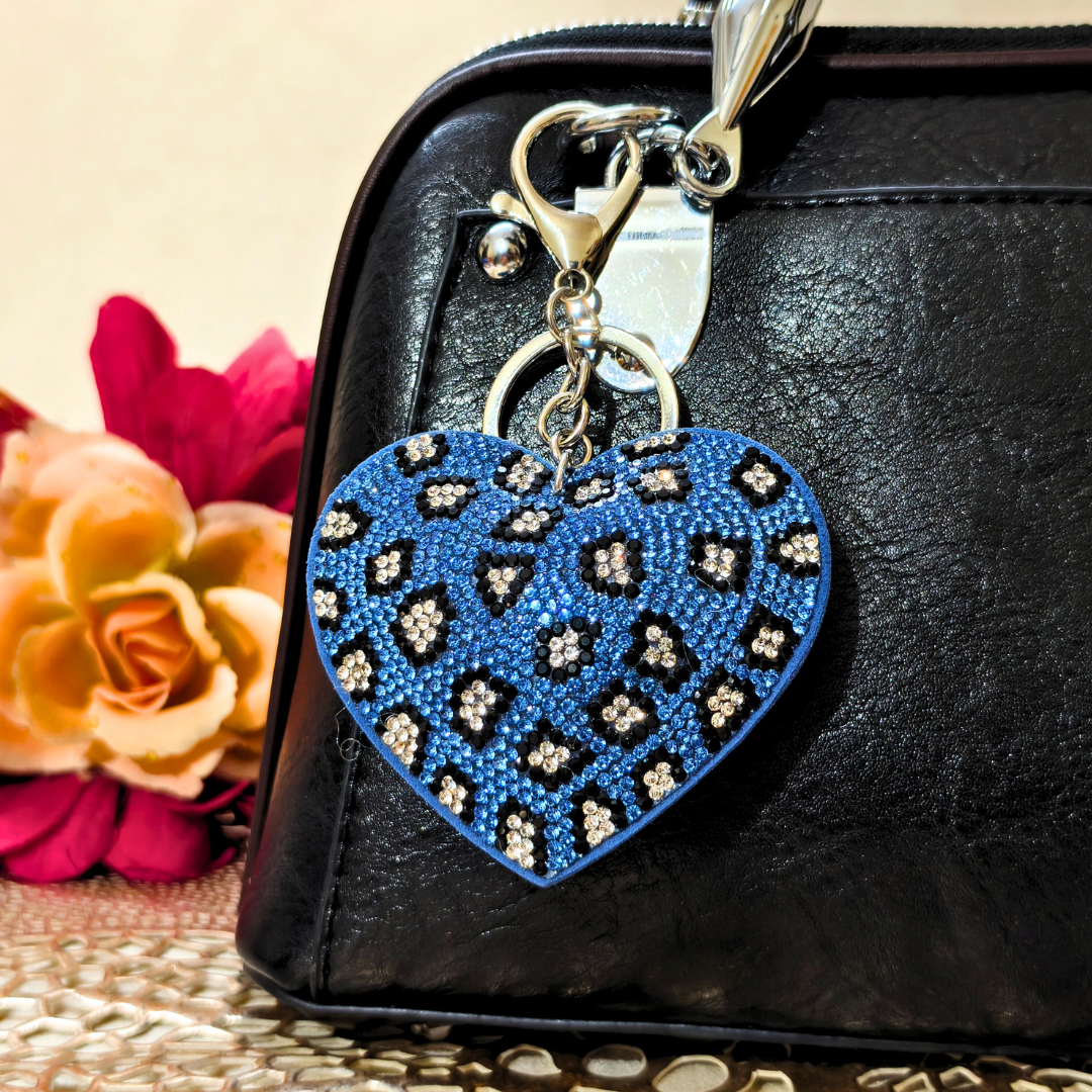 Blue heart-shaped keychain with floral patterns on a black surface with flowers in the background