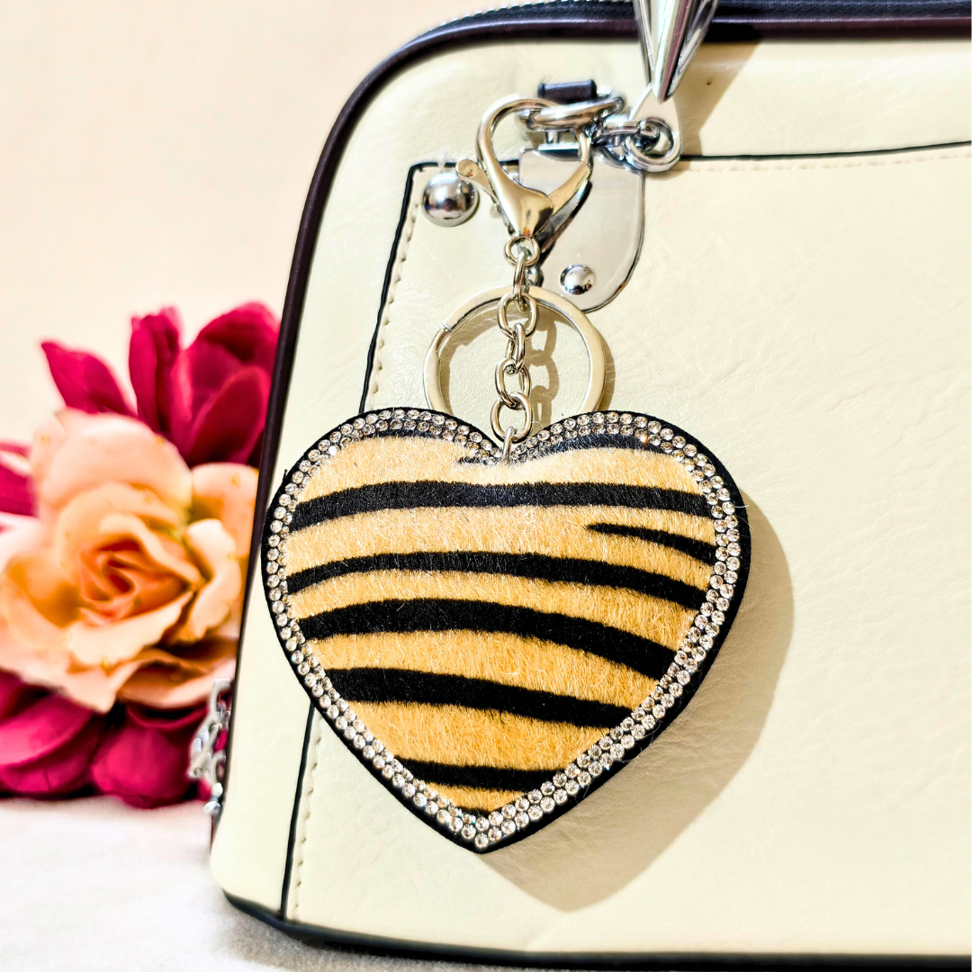 Heart-shaped keychain with zebra pattern on a beige handbag with flowers in the background