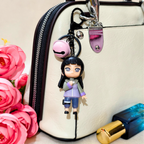 Keychain with a character attached to a handbag next to pink flowers and a lipstick.