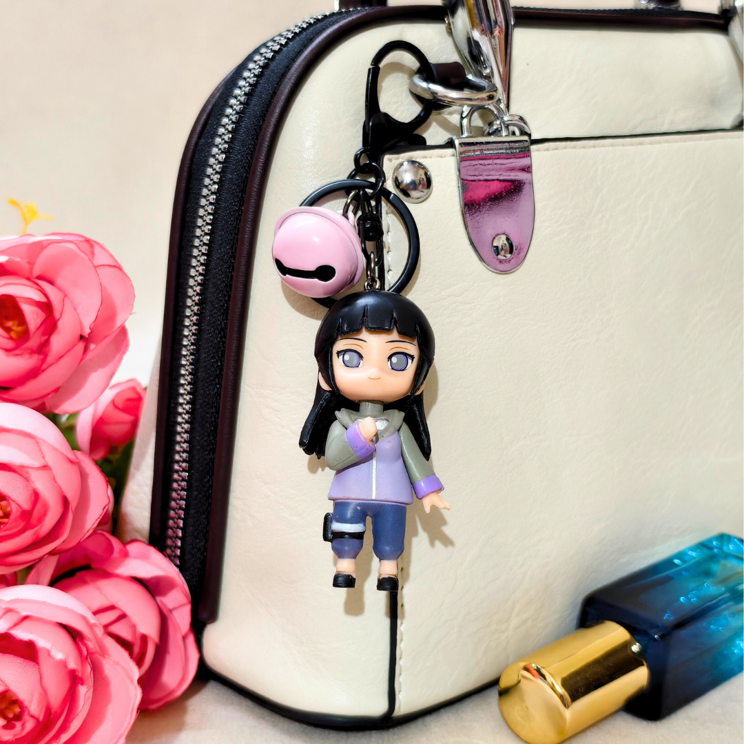 Keychain with a character attached to a handbag next to pink flowers and a lipstick.